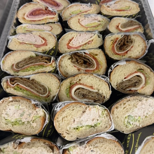 A catering tray filled with various sliced sandwiches, including meat, cheese, and chicken salad.