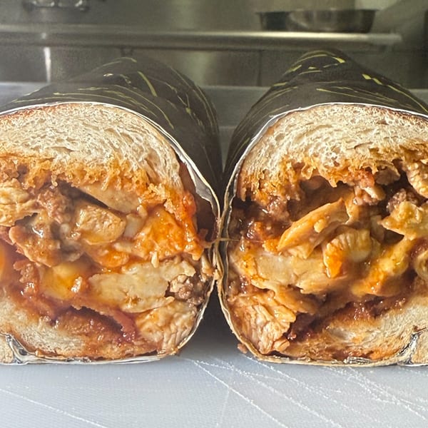 Two halves of a Joe Beez deli sub, filled with saucy chicken and wrapped in foil.