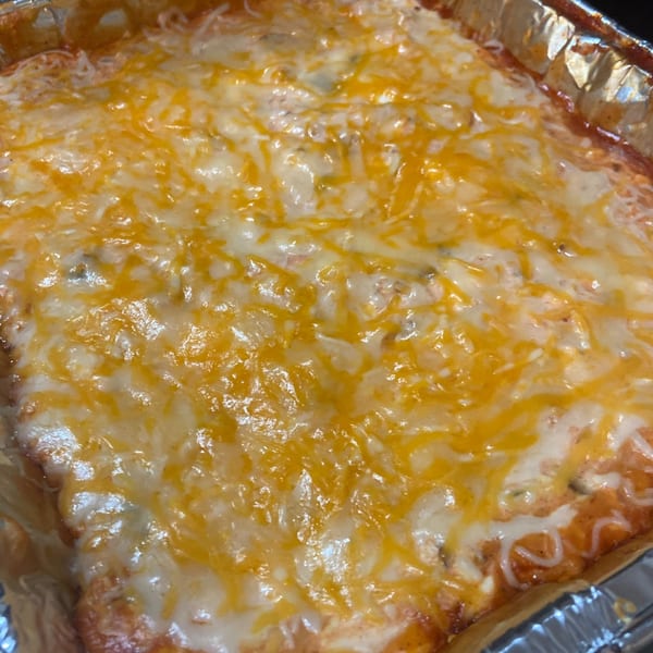 Close-up of a cheesy baked dish, possibly lasagna or enchiladas, in a foil pan.