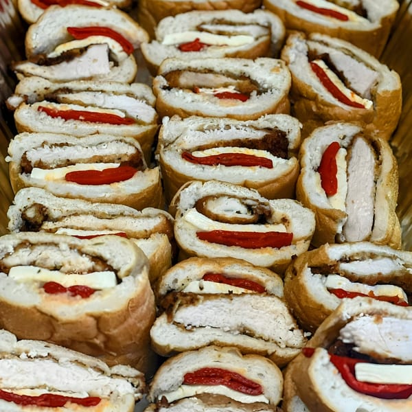 Rows of Joe Beez deli sandwiches, sliced to show chicken, cheese, and red peppers.