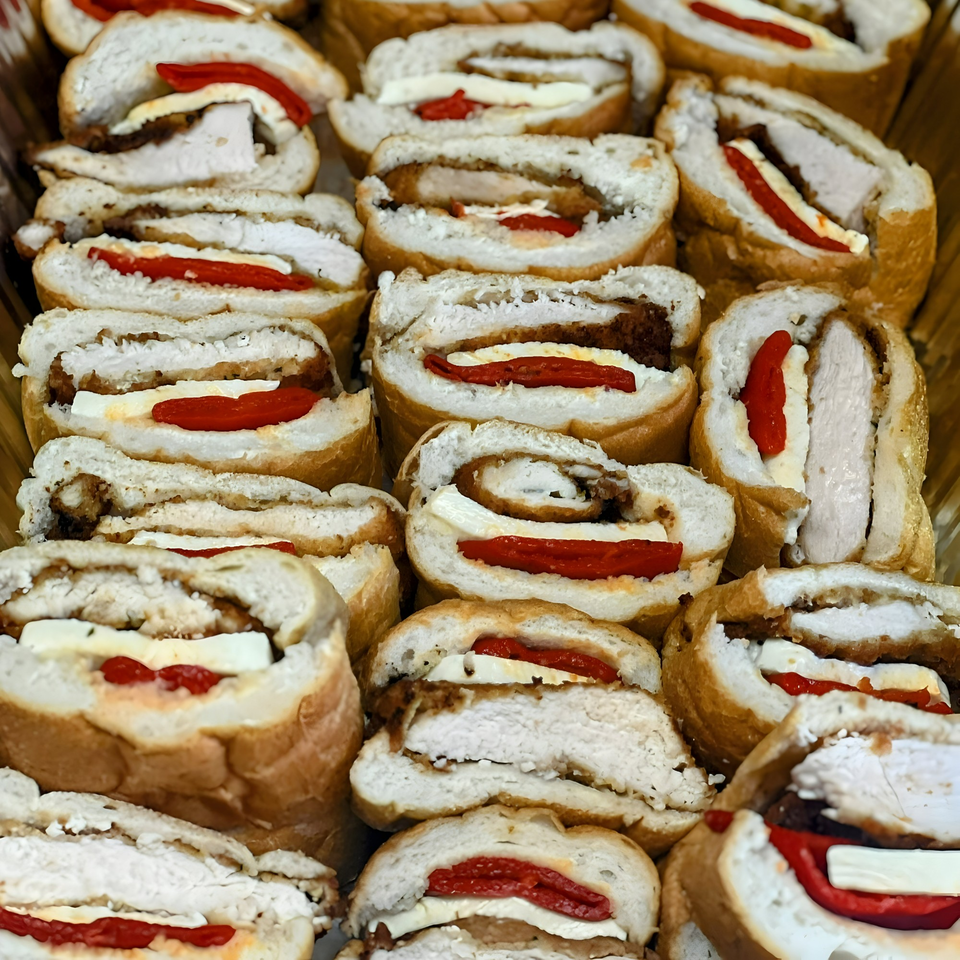 Rows of Joe Beez deli sandwiches, sliced to show chicken, cheese, and red peppers.