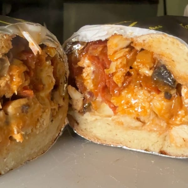 A Joe Beez deli burrito, cut in half, revealing a hearty filling of chicken, rice, and sauce.