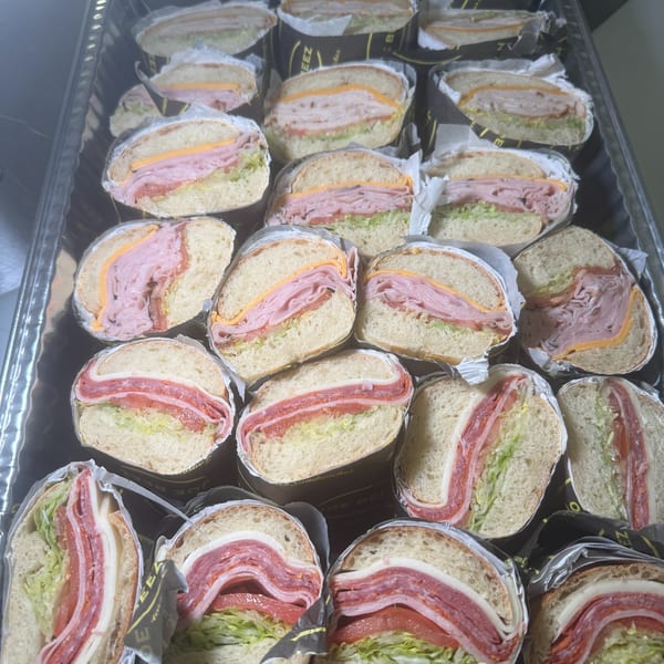 A catering tray filled with individually wrapped sandwiches, some with ham and cheese, others with salami.
