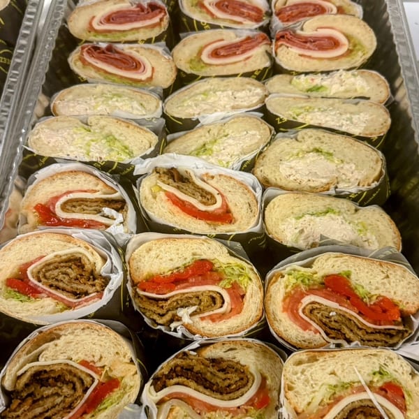 A catering tray filled with various sliced sandwiches, including meat, cheese, and vegetable fillings.