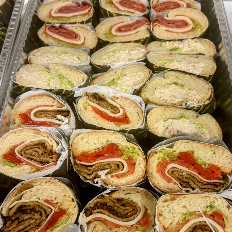 A catering tray filled with various sliced sandwiches, including meat, cheese, and vegetable fillings.