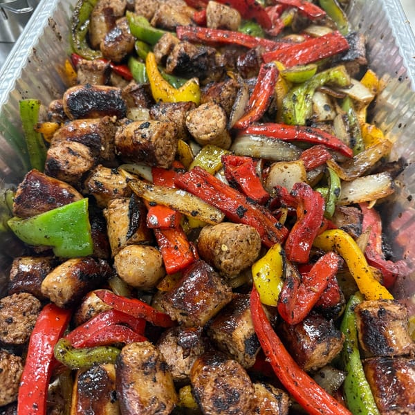 Grilled sausage and peppers, including red, yellow, and green bell peppers, in a metal tray.