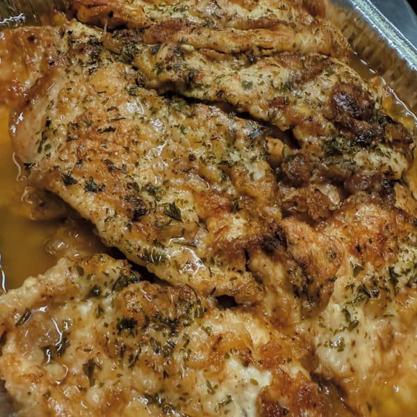 Close-up of golden-brown chicken cutlets with herbs in a pan, from Joe Beez deli.