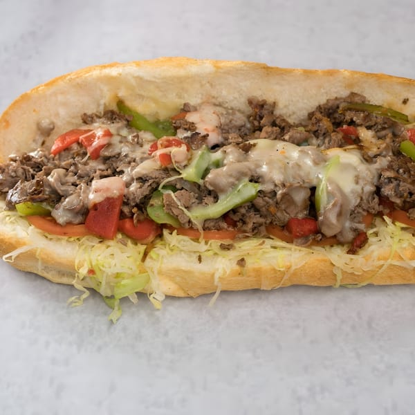 Joe Beez deli cheesesteak with melted cheese, steak, peppers, tomatoes, and shredded lettuce on a sub roll.