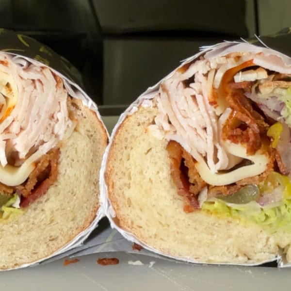 A Joe Beez deli sandwich, cut in half, revealing turkey, bacon, cheese, and lettuce.