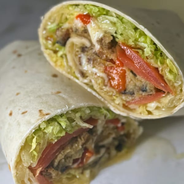 Two halves of a Joe Beez deli wrap, filled with meat, cheese, lettuce, and red peppers.