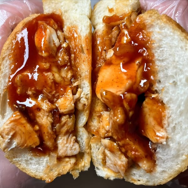 A Joe Beez deli sandwich, cut in half, filled with chicken and a rich, glossy orange sauce.