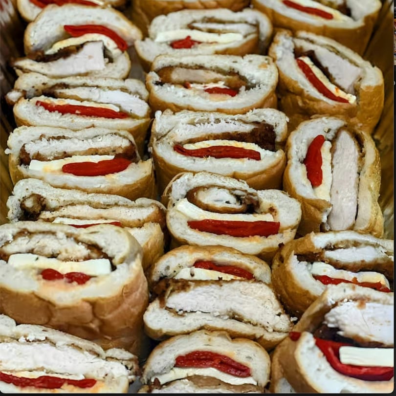 Close-up of numerous sliced chicken and red pepper rolls, showcasing their fillings and golden-brown crusts.