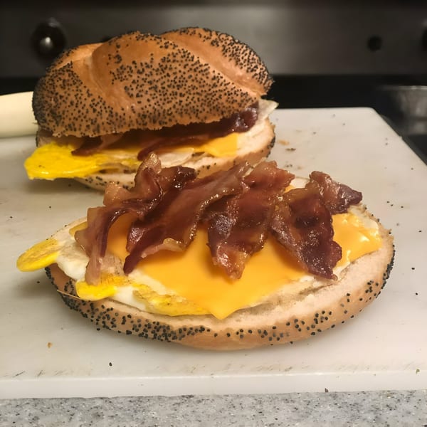 Two Joe Beez deli breakfast sandwiches with bacon, egg, and cheese on poppy seed rolls.
