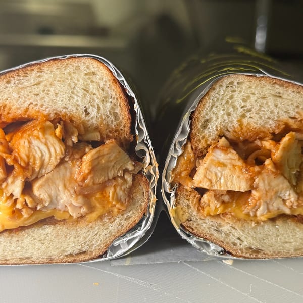 A Joe Beez deli sandwich, cut in half, revealing chicken and cheese on a roll.