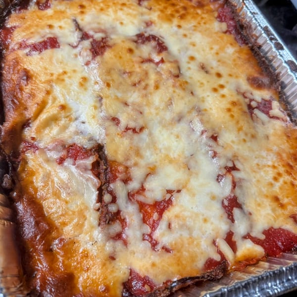 A close-up of Joe Beez's baked lasagna, bubbling with melted cheese and rich red sauce in a foil pan.