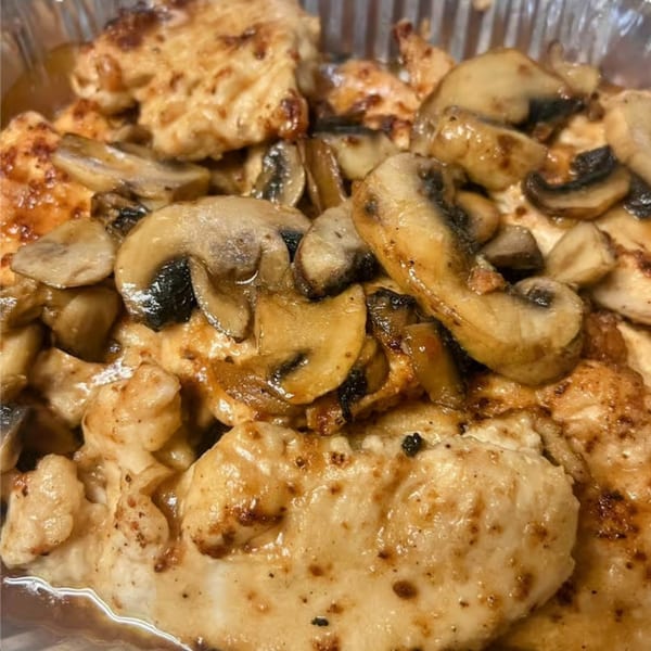Close-up of golden-brown chicken pieces topped with sautéed sliced mushrooms in a foil container.